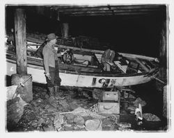 Fishermen inspecting their damaged boat washed ashore under a dock, Bodega Bay, California, January 1959 (Digital Object)
