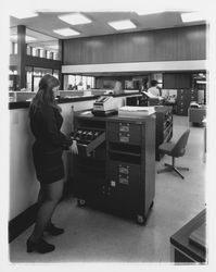 Exchange Bank staff member works at a mobile bill cabinet at the Coddingtown office of the Exchange Bank, Santa Rosa, California, 1972 (Digital Object)