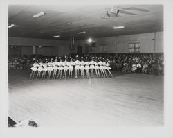 Line of skaters in white tunics and French military style hats in the Skating Revue of 1957, Santa Rosa, California, April, 1957 (Digital Object)